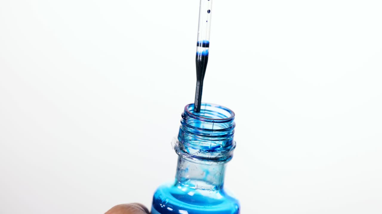 Pipette releases blue food coloring into clear liquid, close-up, bright white background, static shot