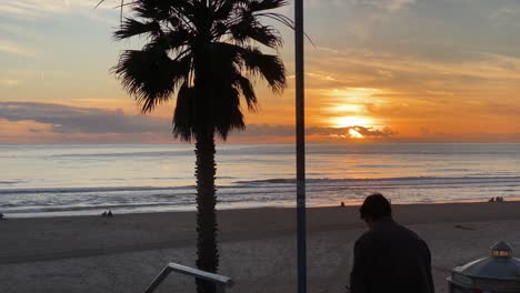 Junger-Mann,-Der-Raucht-Und-Den-Sonnenuntergang-Mit-Blick-Auf-Das-Meer-Und-Die-Wolken-Genießt