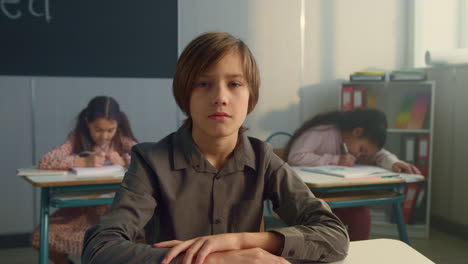 serious schoolboy looking at camera in classroom. focused kid sitting at table