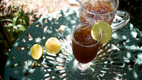 tall glass of ice tea with lemon in outdoor summer garden wind blowing leaves shadows