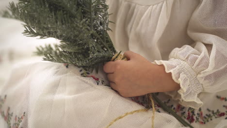 toma en cámara lenta de una joven sosteniendo una rama de adorno navideño de pino con un vestido festivo blanco - de cerca