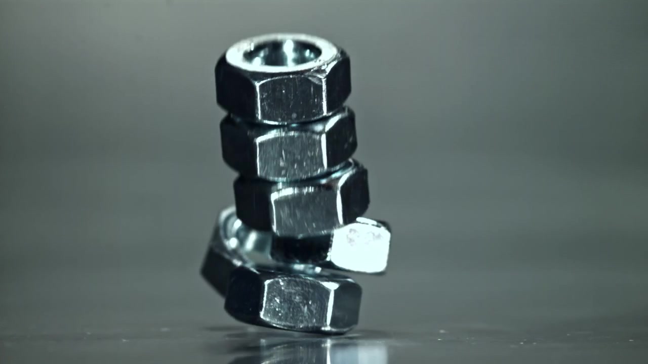 スローモーションで落下し散らばる金属ナットのクローズアップ