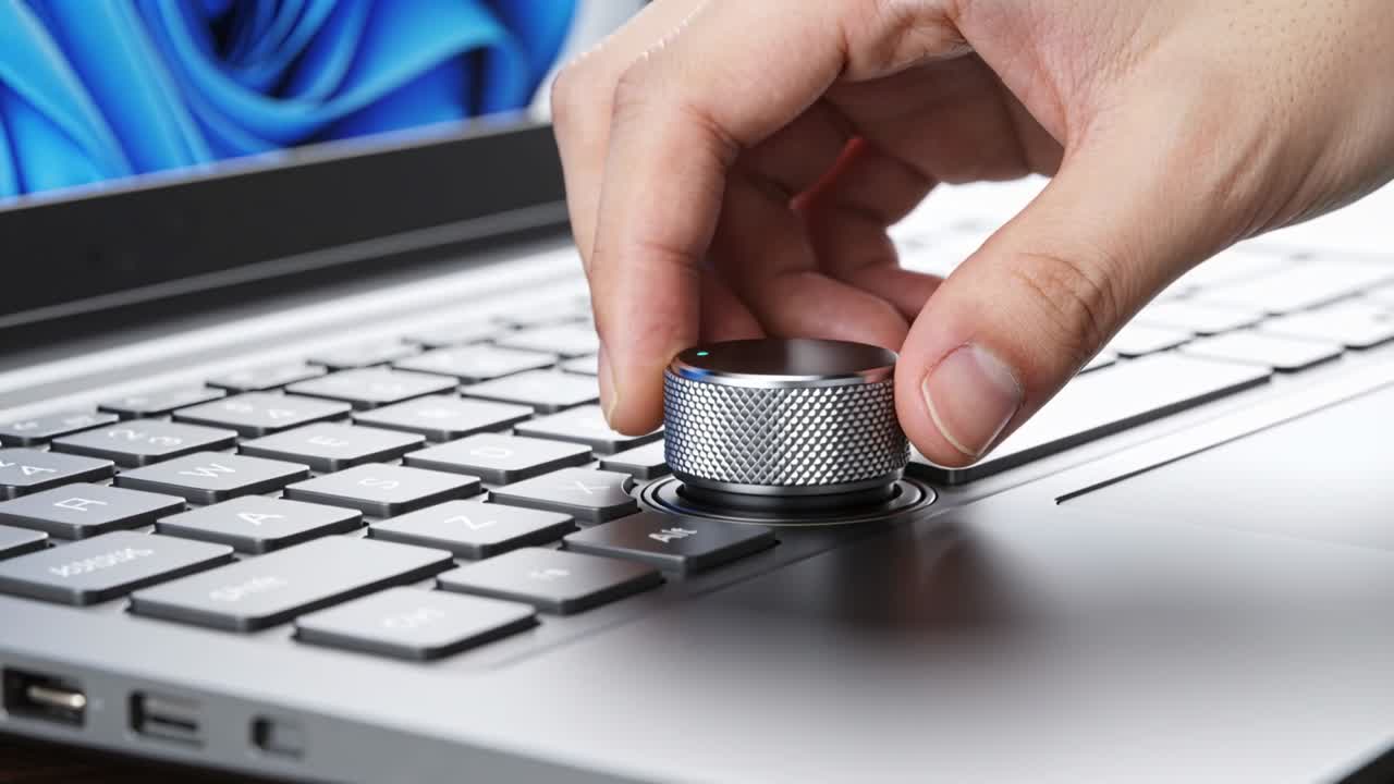 Right hand entering, turning metal dial with green LED on laptop, adjusting volume for technology