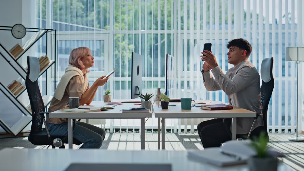 Relaxed colleagues using cellphones sitting desk. Coworkers discussing internet