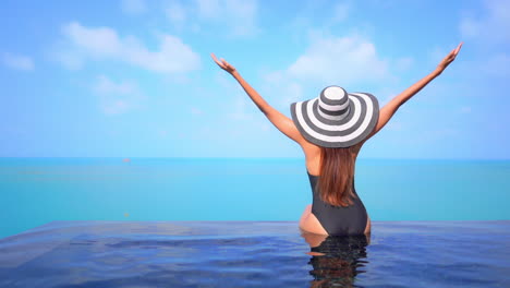 A-sexy-woman-sitting-on-the-invisible-infinity-edge-of-a-resort-pool-while-looking-out-at-the-ocean-beyond