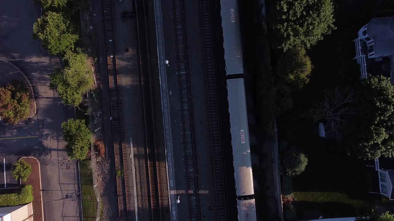 A MBTA red line passenger train seen from overhead as it approaches a station in a residential neighborhood
