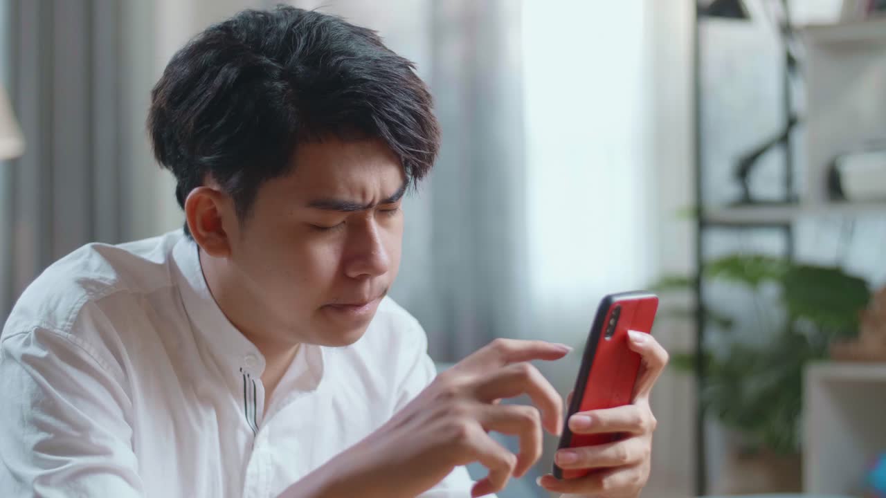 Close Up Side View Of Asian Man Being Tired While Using Smartphone In The Living Room