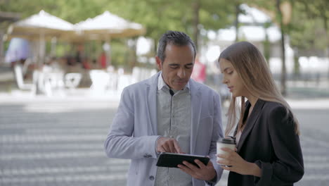 compañeros felices de sexo masculino y femenino que usan tablets al aire libre