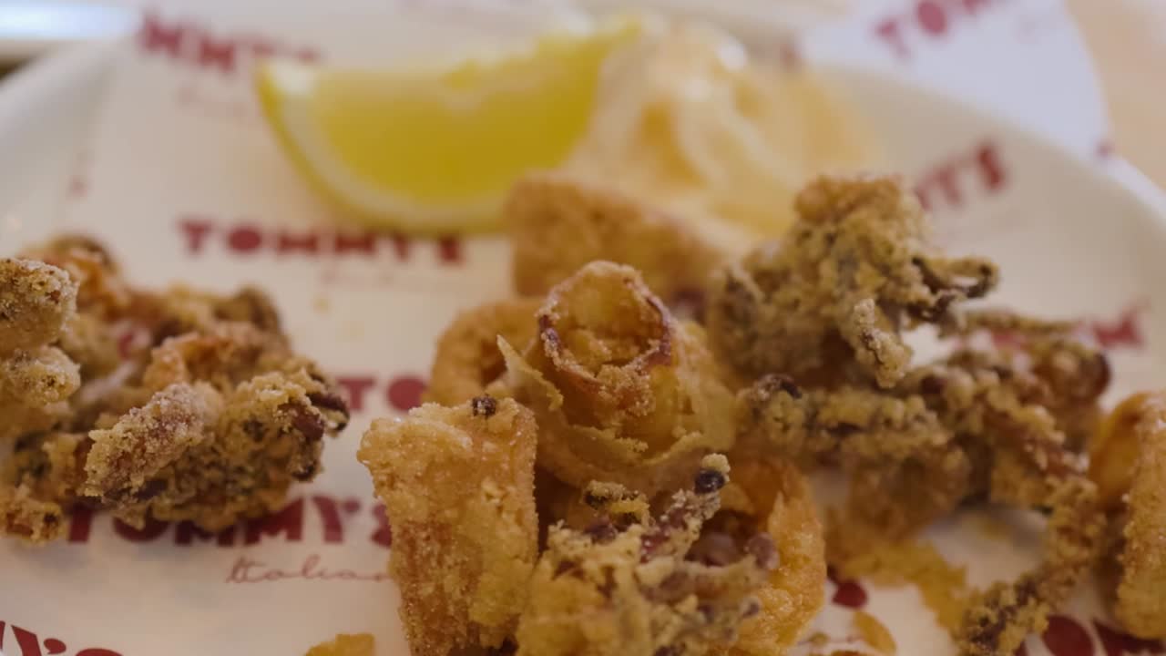 Uno scatto ravvicinato dettagliato di anelli di calamari fritti dorati, serviti con limone e salsa.