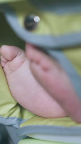 little baby sits in green highchair and funny child bare feet look out against mother dress extreme close view