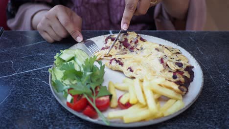 woman enjoying a delicious omelette with french fries and salad