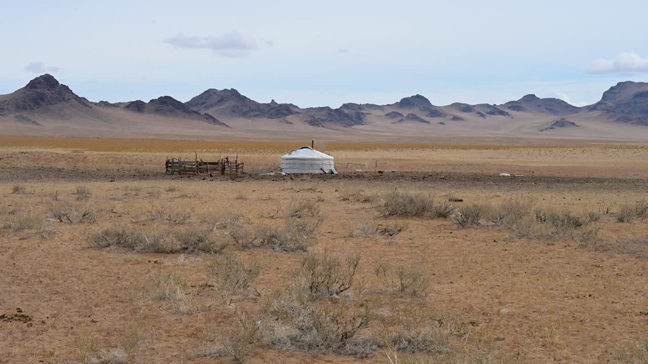 An eagle soars over a lone ger and corral on the vast Mongolian steppe, with a rugged mountain range behind. A powerful scene of nature and nomadic life