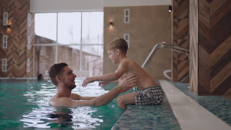 father is teaching son to swim in swimming pool of modern wellness spa healthy lifestyle