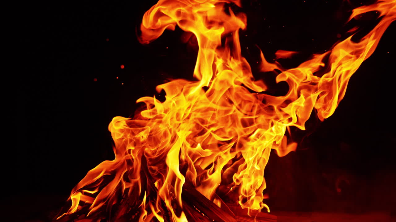 Big bonfire burning and producing a cloud of sparks flying up. Campfire close up at night.