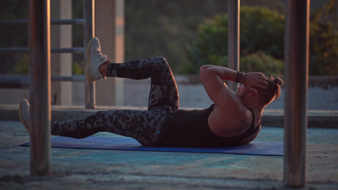 Uomo in forma che esegue crunch a bicicletta su tappetino da yoga al tramonto.