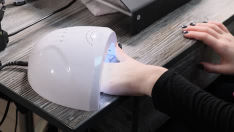 woman dries nails under a special lamp for drying nails