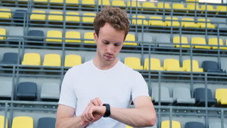 Glücklicher-Sportlicher-Mann,-Der-Vor-Dem-Outdoor-Training-Im-Stadion-2-Seine-Smartwatch-überprüft