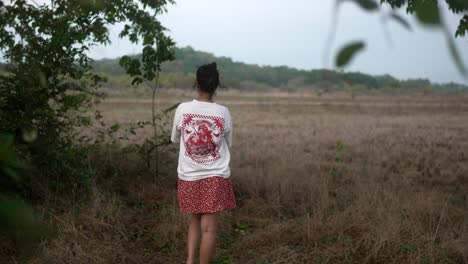 A-woman-stands-alone-in-a-field-wearing-a-white-shirt-and-red-skirt-during-a-calm-day