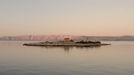 Aerial-shot-of-a-small-island-in-Croatia-in-the-middle-of-the-sea-during-sunrise,-clear-view-of-the-Adriatic-sea-during-blue-hour,-Sveti-Marin-Chapel,-Novi-Vinodolski,-beautiful-travel-destination