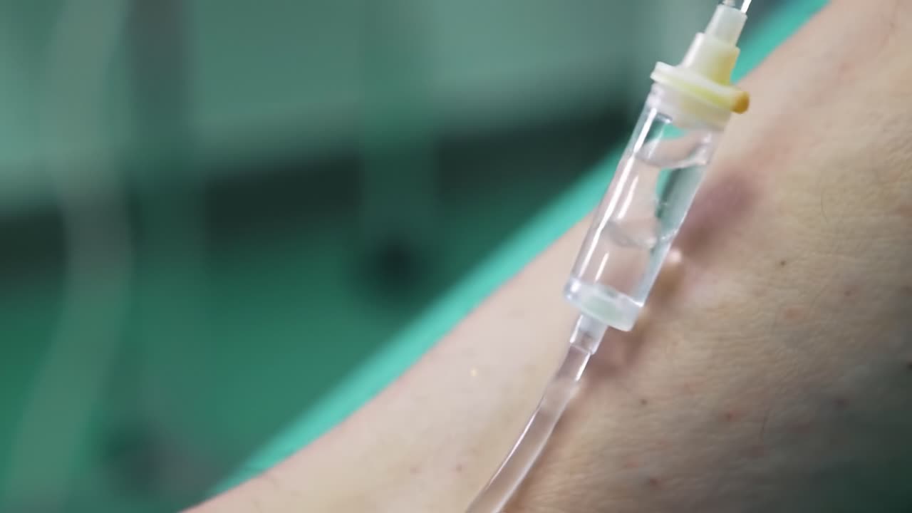 Close-up of an arm with an intravenous drip, reflecting the medical care being administered in a hospital. The setting emphasizes patient comfort and monitoring during treatment.