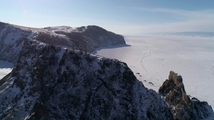 воздушный наклонный снимок мыса хобой, остров олхон. высокие скалы в замерзшем озере байкал с большим количеством людей и автомобилей вокруг. популярное туристическое направление. зимний пейзаж. панорамный вид