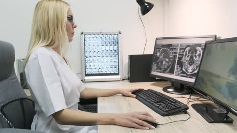 professional female doctor radiologist examines brain ct or mri scan results, working on a computer screen at her personal desk at hospital