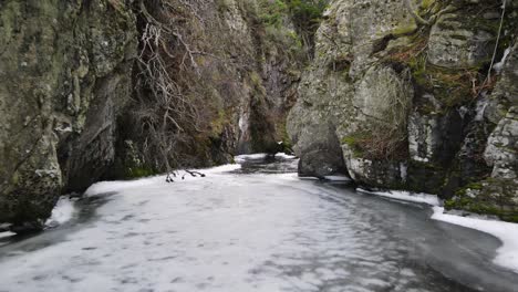 Frozen-river-between-rocks-and-bushes