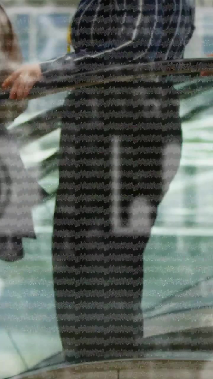 Vertical video: Two commuters walking, other coming, both pausing and resting hands on lined glass