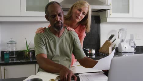 concerned diverse senior couple using laptop computer paying bills in kitchen