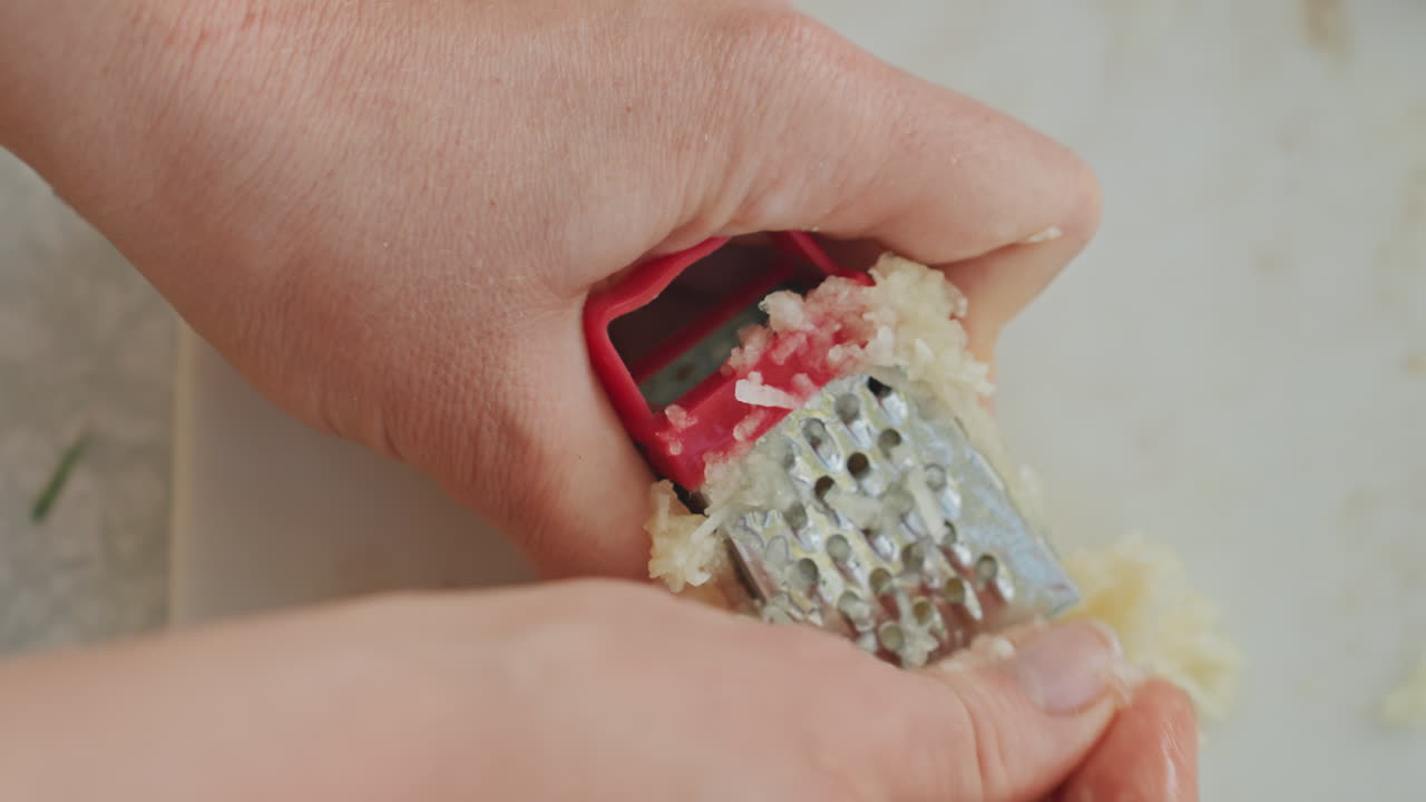 Dimostrazione di grattugia per aglio all'aperto. Affettatura precisa dell'aglio con una grattugia manuale all'aperto. Processo dettagliato di grattugiare l'aglio manualmente su una superficie esterna per la preparazione di un pasto fresco.