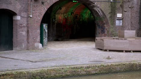 Underpass-archway-with-urban-graffiti-and-changing-rainbow-coloured-lights,-viewed-from-a-canal-boat-cruising-along-the-Utrecht-canals-in-the-Netherlands