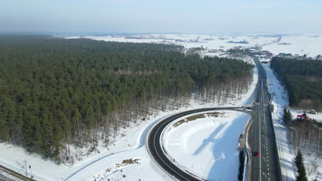 Vehículos-Que-Viajan-Por-La-Carretera-Y-La-Carretera-Curva-Con-Bosque-Verde-En-El-Campo-Nevado-En-Rakowice,-Cracovia,-Polonia