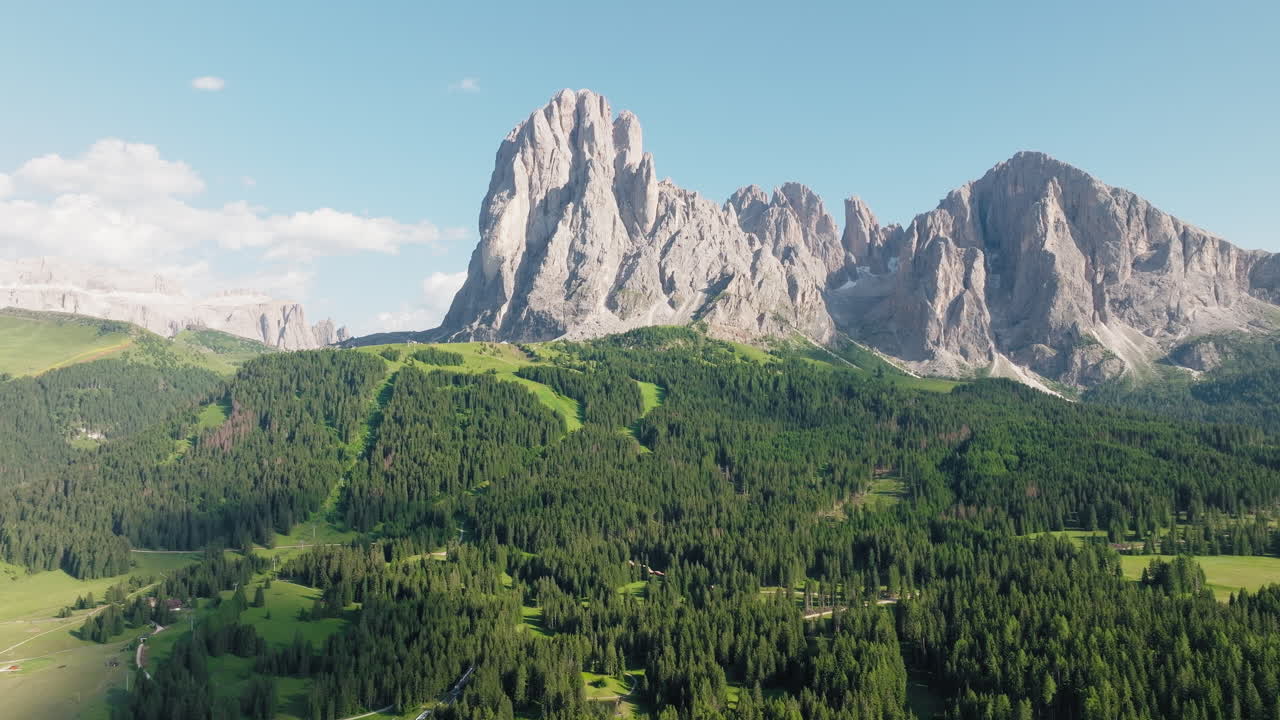 Drone establishing of Langkofel mountain range surrounded by rolling meadows and forest trail