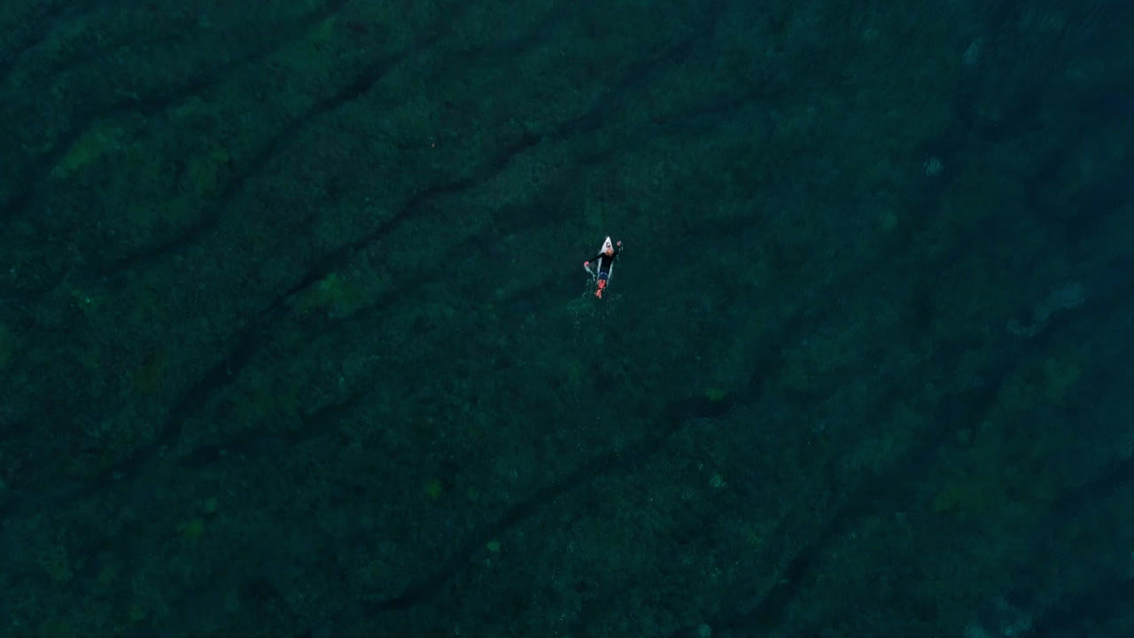 Drone top down rises above surfer paddling above reef