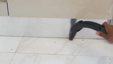 a person using a vacuum cleaner to clean up crumbs on a tiled kitchen floor