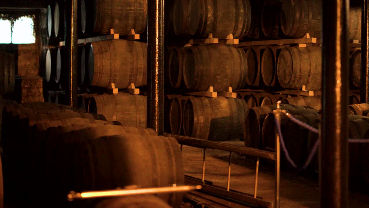 Panorâmica com câmera e iluminação quente revela barris de madeira empilhados dentro de um armazém tradicional de whisky escocês