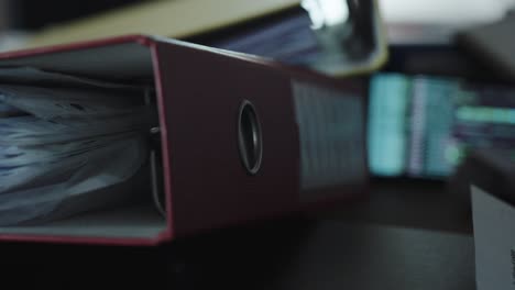 A full folder in the foreground, with a blurred AI-generated code running on a screen in the background – a symbolic image of the digital transformation in the workplace