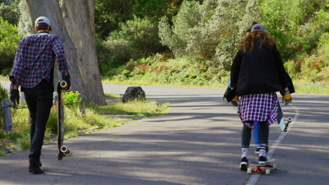 rear view of cool young caucasian male skateboarders walking with skateboard at countryside road 4 4