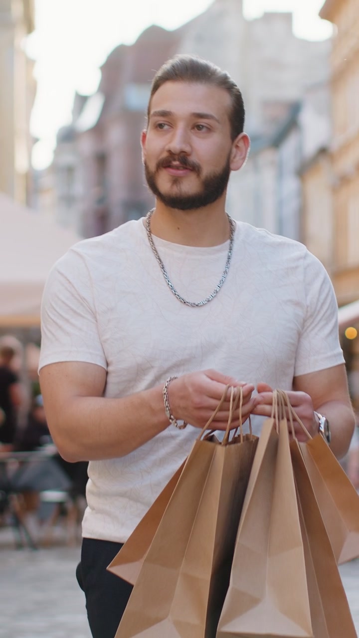 Felice giovane uomo, acquirente compulsivo, dopo i saldi, con borse piene, che cammina per la strada in città.