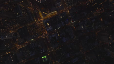 Aerial-birds-eye-overhead-top-down-panning-view-of-busy-roads-in-evening-city.-Illuminated-contour-of-modern-skyscraper.-Manhattan,-New-York-City,-USA