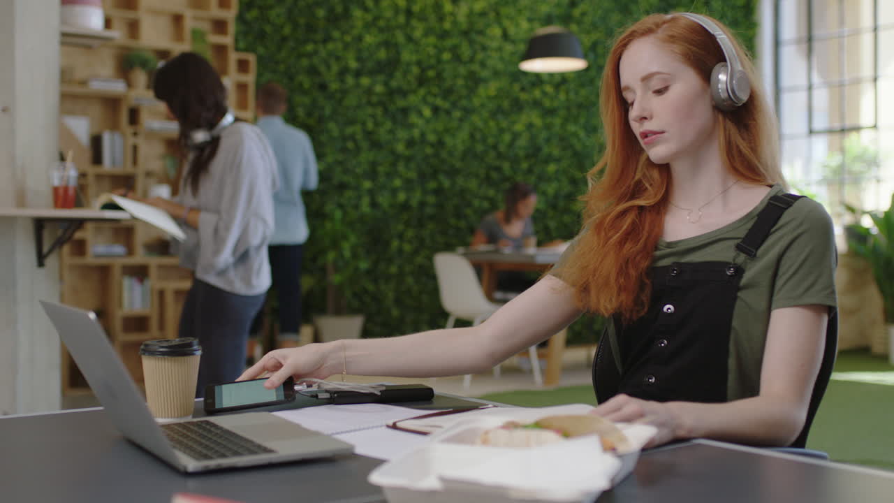 молодая кавказская бизнес-леди пишет заметки, наслаждается учебой, слушает музыку, носит наушники, студентка использует смартфон, проверяет сообщения в различных офисах на рабочем месте