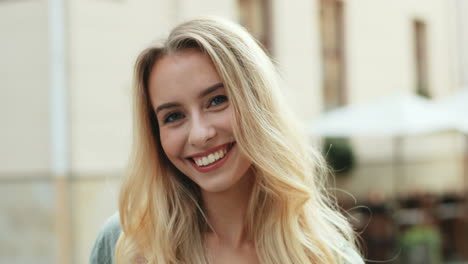 close-up view of blonde young woman smiling at the camera while standing in the street