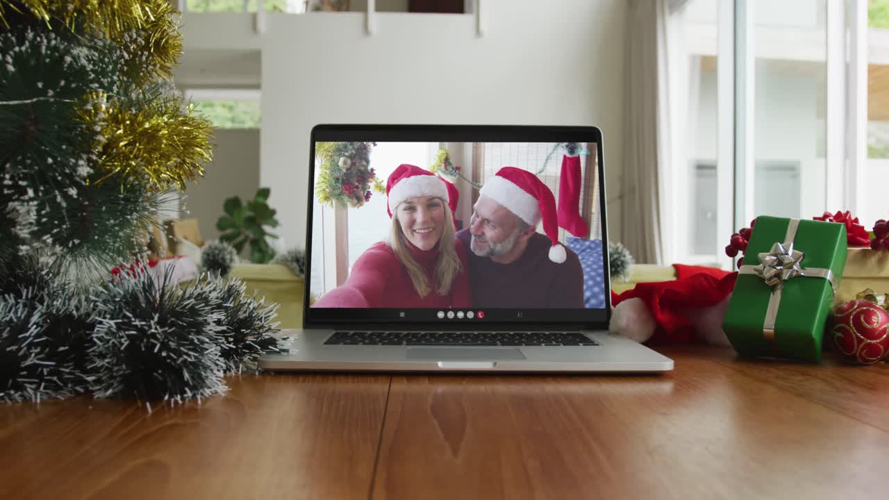 una pareja caucásica sonriente con sombreros de santa claus en una videollamada de navidad en una computadora portátil