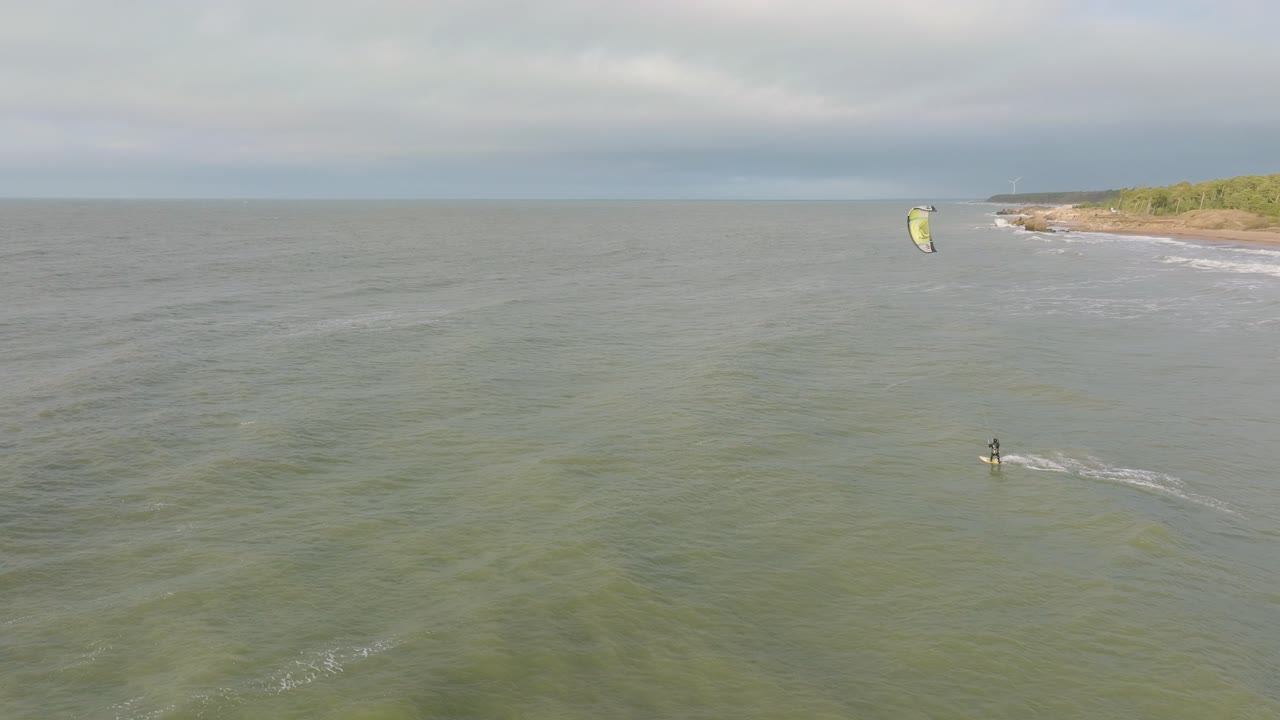 establecimiento de una vista aérea de un grupo de personas dedicadas al kitesurf, día de invierno nublado, olas altas, deporte extremo, playa de karosta del mar báltico, amplio tiro de drones avanzando