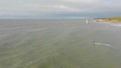 Establishing-aerial-view-of-a-group-of-people-engaged-in-kitesurfing,-overcast-winter-day,-high-waves,-extreme-sport,-Baltic-Sea-Karosta-beach-,-wide-drone-shot-moving-forward