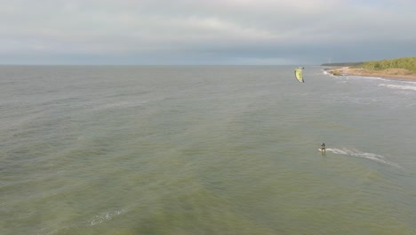 establecimiento de una vista aérea de un grupo de personas dedicadas al kitesurf, día de invierno nublado, olas altas, deporte extremo, playa de karosta del mar báltico, amplio tiro de drones avanzando