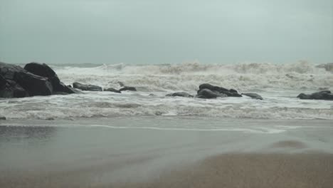 Wellen,-Die-über-Eine-Felsige-Küste-Rollen-Und-Krachen-Und-Sand-Zurückziehen,-Wenn-Das-Wasser-Zurück-Ins-Meer-Fließt