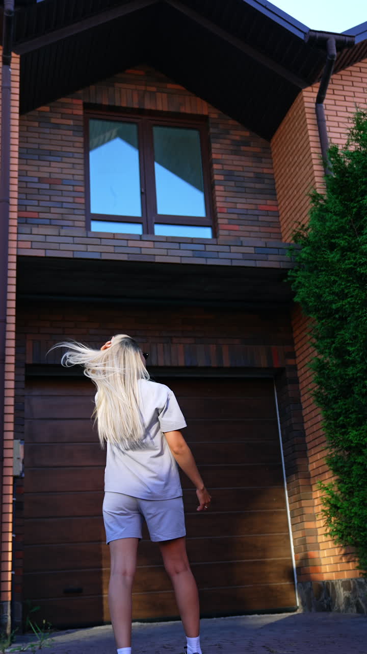 Girl admires house at sunset. A young girl with long blonde hair admires a contemporary house in the evening light