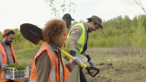 Group-of-multiethnic-ecologist-activists-walking-in-the-forest-while-holding-trees-and-tools-to-reforest