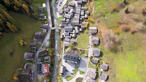 drone flying above swiss village in autumn , fall with mountains and a river on the background